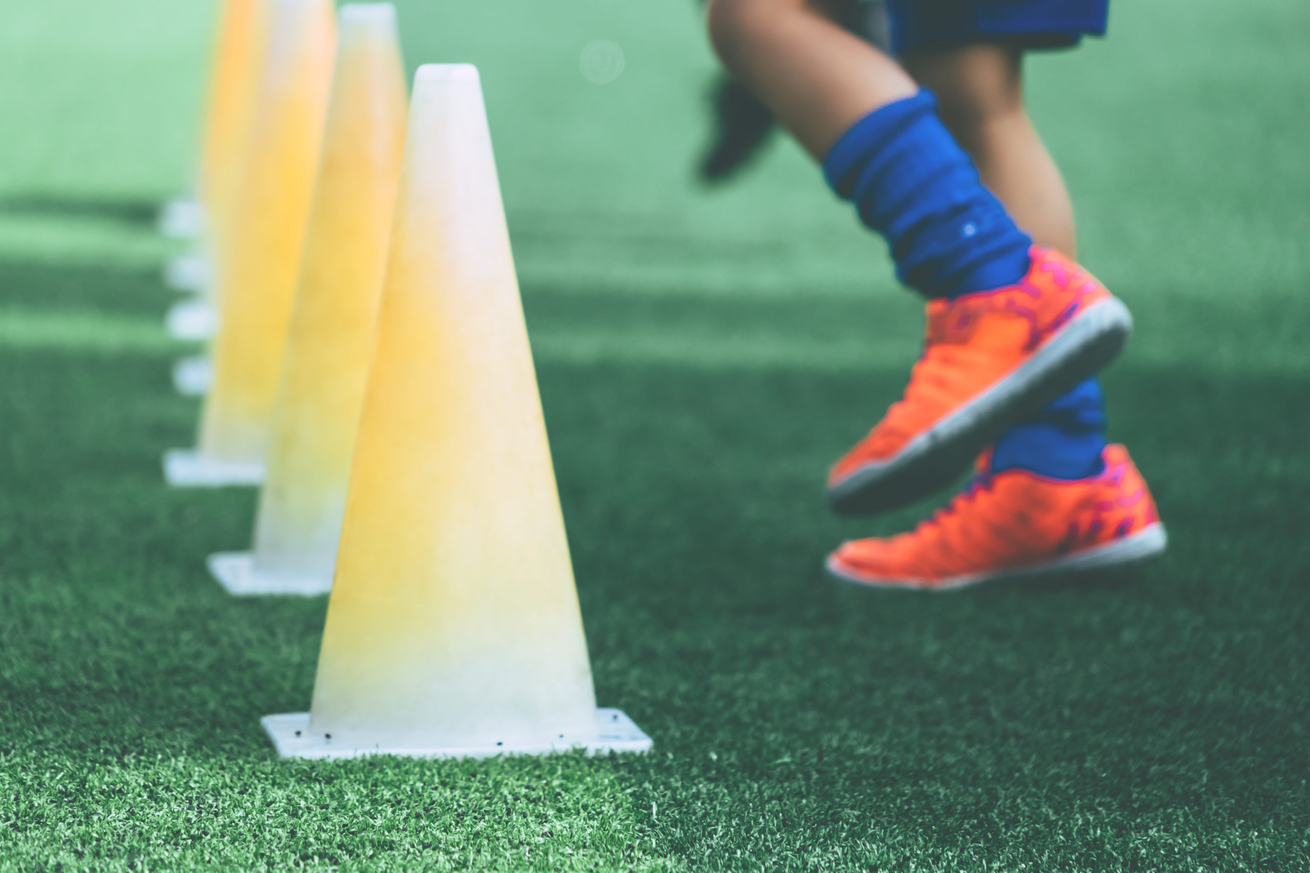 Children feet with soccer boots training on training cone on soccer ground